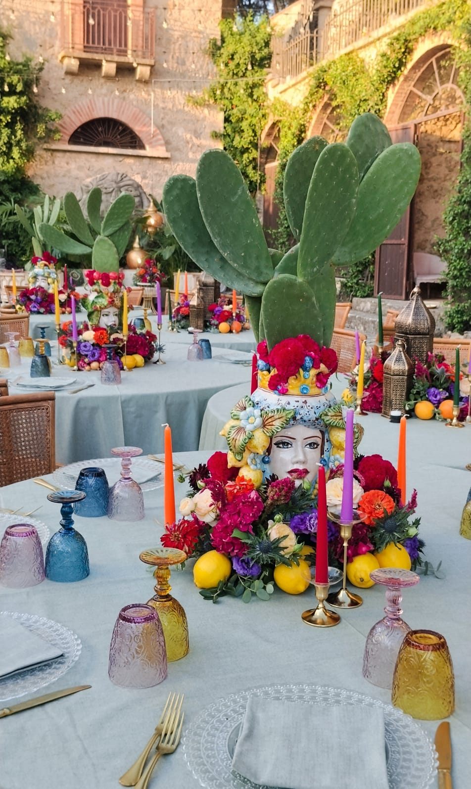 Centrotavola con testa di moro in ceramica, fiori rossi e arancio, limoni e candele colorate