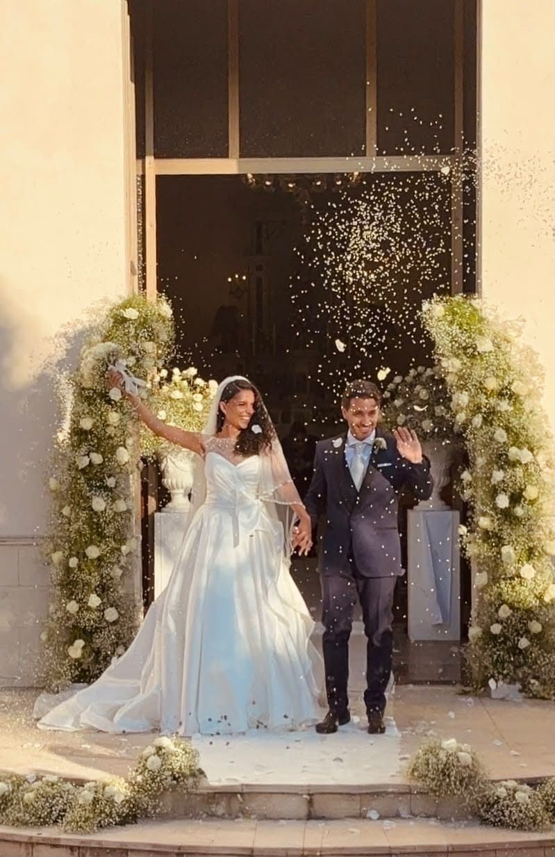 Sposi all'uscita della chiesa sotto una pioggia di riso tra colonne di gypsophila e rose bianche